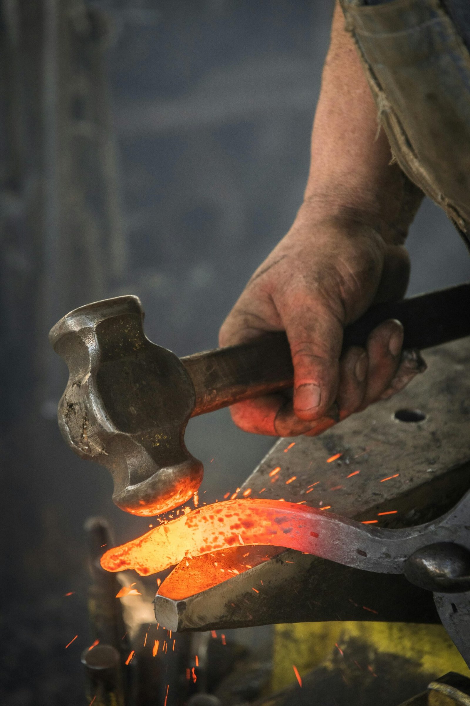 Close-up of a blacksmith hammering a hot iron piece in a workshop.